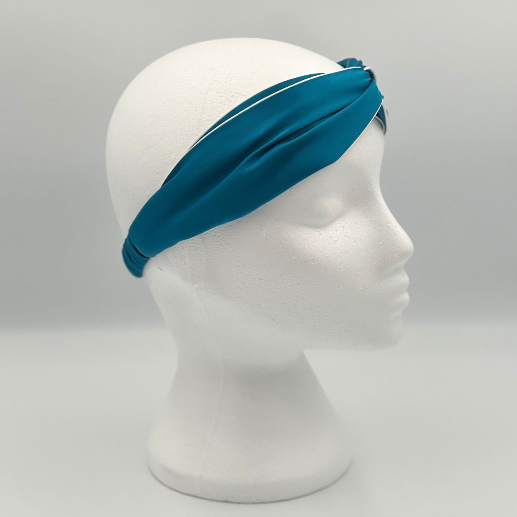 A teal silk headband on a mannequins head. The picture show the side of the headband