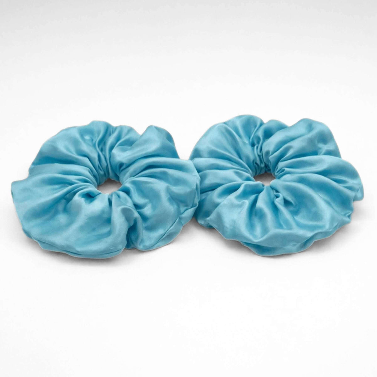 Two light blue jumbo silk scrunchies on a white background
