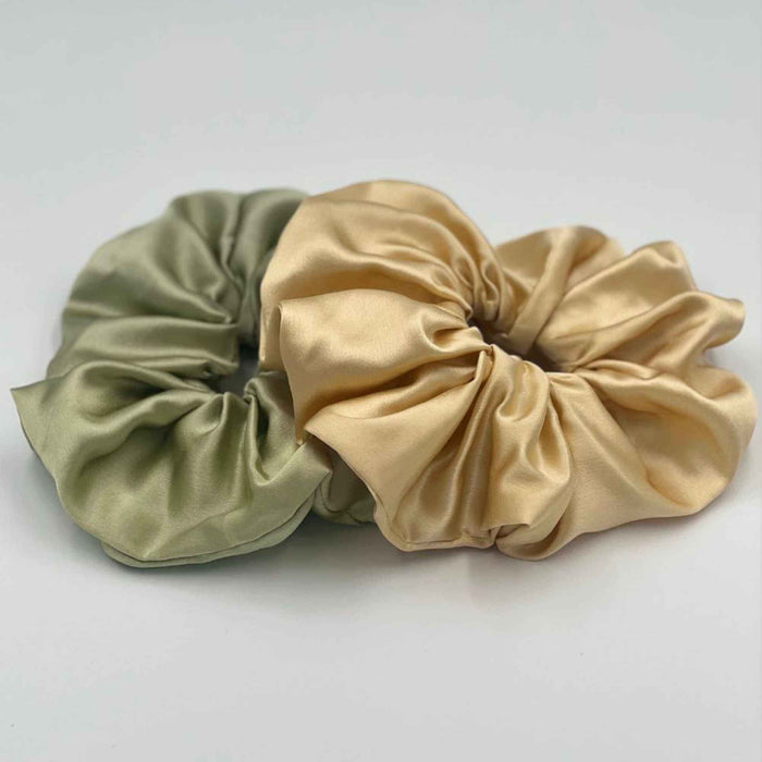 Two mulberry silk oversized scrunchies, one pistachio green and one golden yellow, on a light grey background.